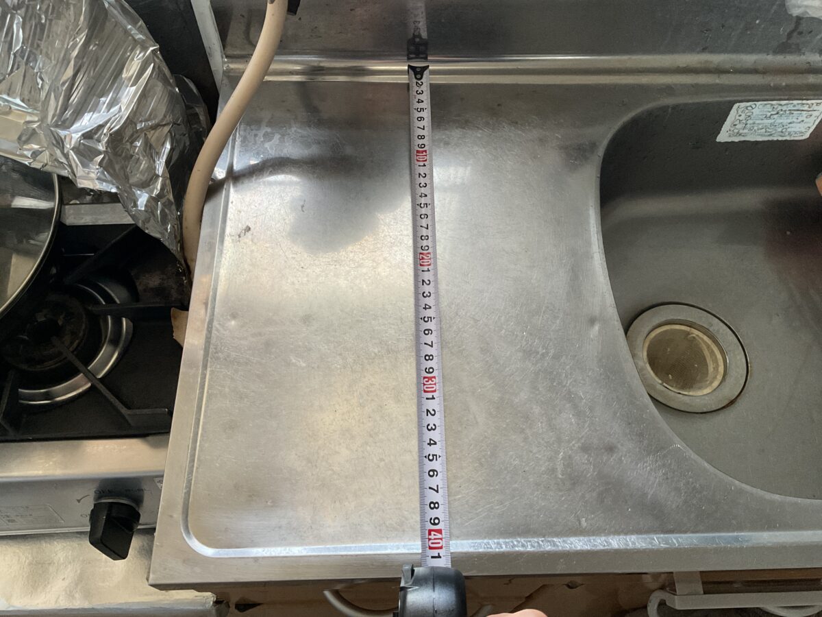 一人暮らしのキッチンで自動調理器の設置を想定して作業台の奥行き約42cmを測っている様子