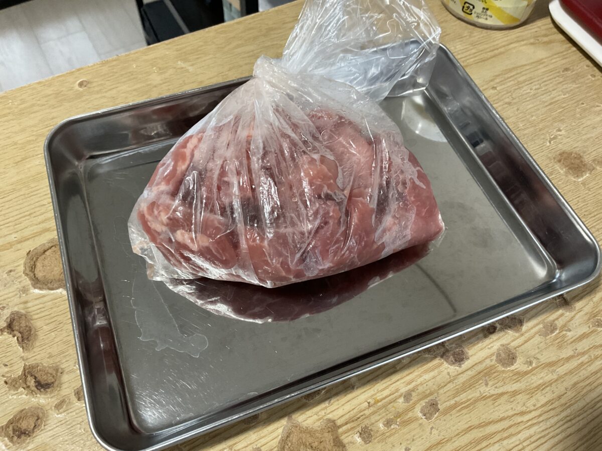 料理用ポリ袋に入れた生肉をステンレス製バットの上で下ごしらえしている様子