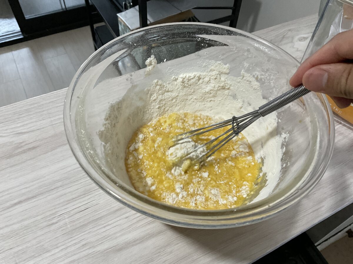 ボウルの中でパウンドケーキの生地と小麦粉を泡立て器で混ぜている様子