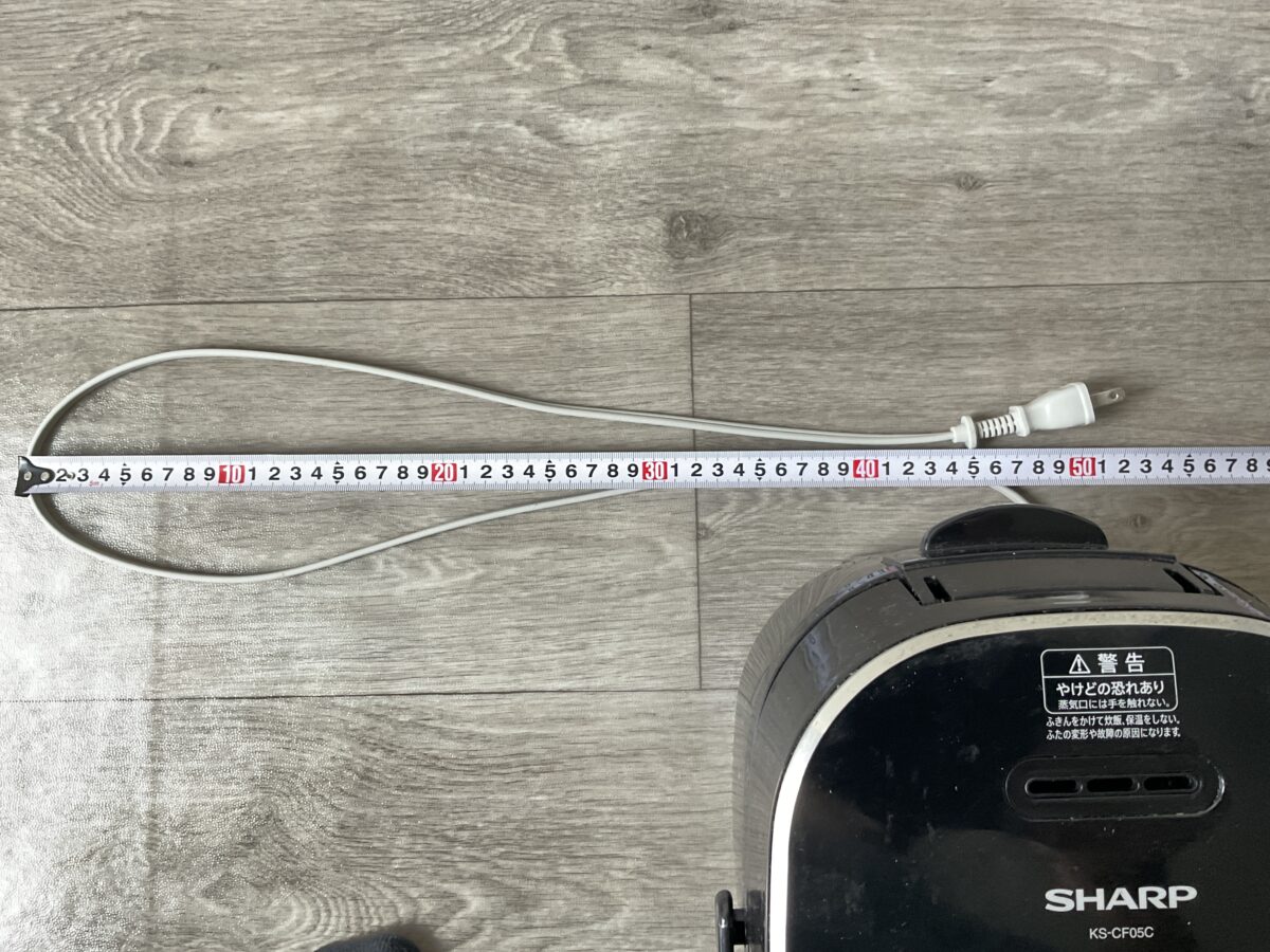 炊飯器の電源コードをメジャーで測り約90cmの長さを確認している様子