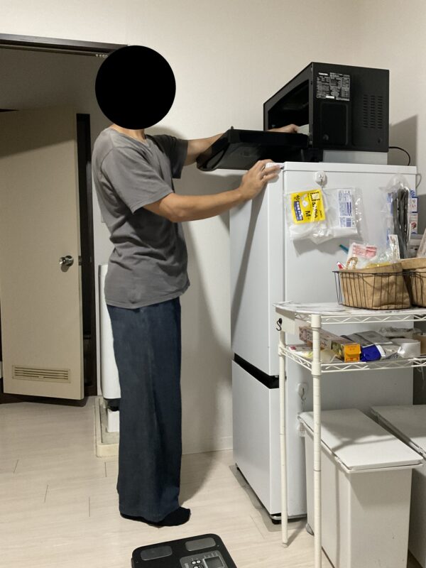 身長約170cmの管理人が、ハイセンスの冷蔵庫HR-D15F(約130㎝)の上に設置した東芝オーブンレンジER-YD70-Kの扉を開け、庫内に手を伸ばしている様子。設置高さや実際に使うときの高さ感が分かります。